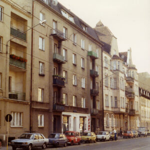 czteropiętrowa, prosta kamienica z balkonami, przed nią stoją zaparkowane samochody