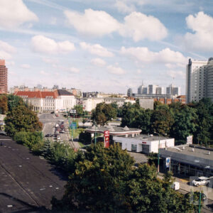 z lotu ptaka fragment ulicy, jeżdżące nią samochody, widoczne dachy niskich budynków