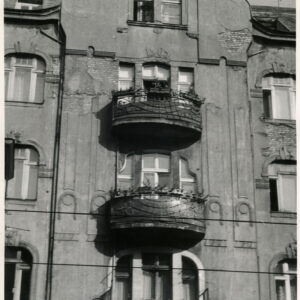 fragment ściany z oknami i balkonami ze zdobionymi balustradami, widoczne ślady cegły po odpadnięciu tynku