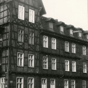 dwupiętrowy dom drewniano-ceglany z użytkowym poddaszem, narożnik z dodatkową kondygnacją, nakrytą stromym dwuspadowym dachem, przed budynkiem zaparkowane samochody