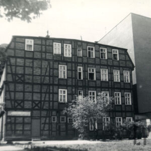 dwupiętrowy dom drewniano-ceglany z użytkowym poddaszem, z prawej fragment otynkowanej ściany bez okien sąsiedniego budynku