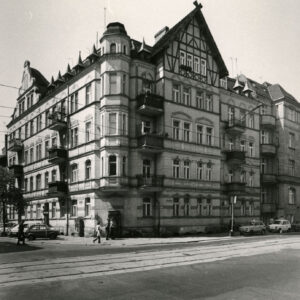 trzypiętrowa kamienica z użytkowym poddaszem, elewacje zwieńczone ozdobnymi szczytami, na pierwszym planie asfaltowa ulica z torami tramwajowymi