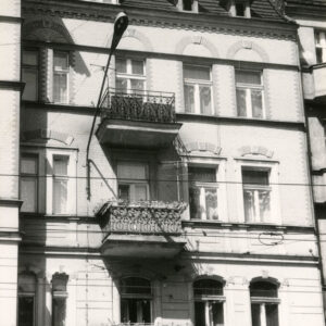 fragment ściany budynku z oknami i balkonami, nad oknami zdobienia