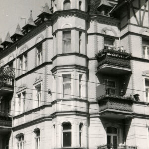 fragment ściany budynku z oknami i balkonami, nad oknami zdobienia