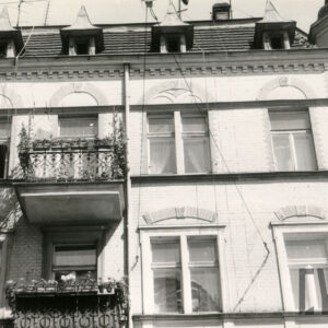 fragment ściany budynku z oknami i balkonami, nad oknami zdobienia