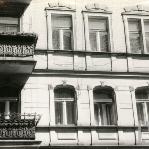 fragment ściany budynku z oknami i balkonami, nad oknami zdobienia