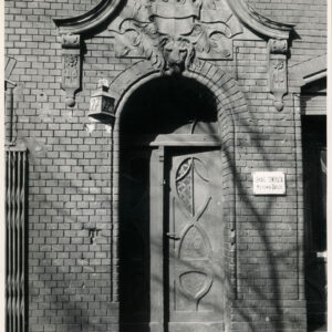 fragment ceglanej ściany z drewnianymi drzwiami, nad nimi bogate zdobienia