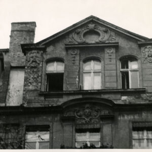 ostatnie piętro kamienicy z trzema oknami i trójkątnym szczytem, dookoła nich bogata dekoracja rzeźbiarska