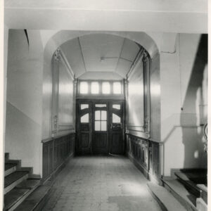 na wprost drewniane drzwi wejściowe do kamienicy, zdobiona posadzka, bogato zdobione ściany sieni, po obu stronach schody