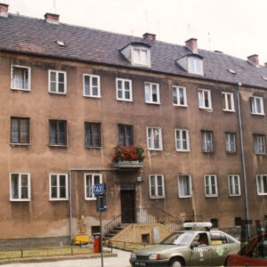 dwupiętrowy, prosty budynek z użytkowym poddaszem, przed budynkiem postój taksówek