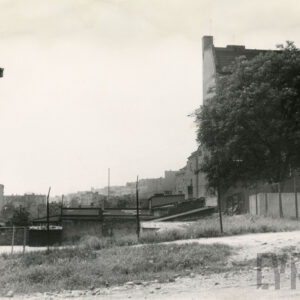 niskie budynki gospodarcze między wielokondygnacyjnymi, murowanymi budynkami mieszkalnymi, ogrodzone ogrodzeniem z metalowej siatki