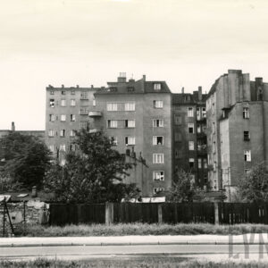 kilkukondygnacyjne, murowane, otynkowane kamienice mieszkalne, na pierwszym planie drewniany płot