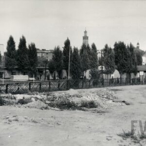 za drewnianym ogrodzeniem baraki, w głębi wieża kościoła