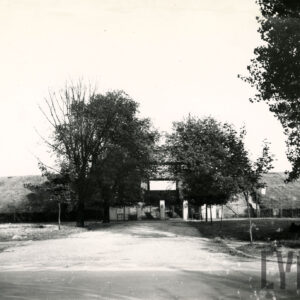 asfaltowa droga prowadząca do przejścia w gruntowym nasypie, po obu stronach wejścia rosną drzewa