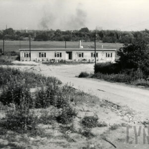 teren gruntowy z krzakami, w głębi parterowy, długi murowany budynek
