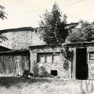 z przodu z lewej drewniane komórki gospodarcze, z prawej budynek ceglany, w głębi ceglana ściana