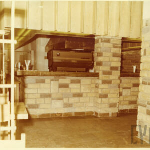 wnętrze baru z drewnianymi, prostymi meblami i ścianami wyłożonymi nieregularnymi, kamiennymi płytkami