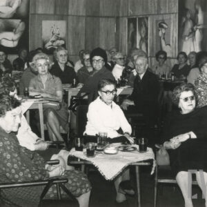 starsze osoby, kobiety i mężczyźni, siedzą w fotelach i na krzesłach przy stolikach, na ściennej boazerii wiszą obrazy