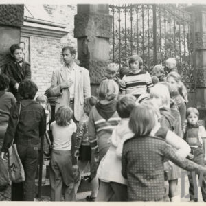 grupa dzieci przed kutą, metalową bramą prowadzącą prawdopodobnie do ceglanego kościoła