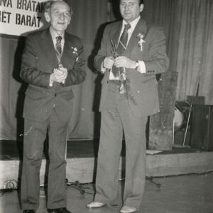 dwóch mężczyzn w garniturach, za nimi fragment napisu w języku polskim i węgierskim