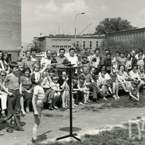 duża grupa dzieci i dorosłych, część z nich siedzi na ławkach, część stoi