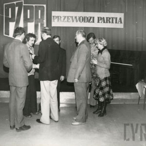 grupa ludzi stoi, za nimi dwie plansze z napisami „PZPR” wpisane w kontur Polski, obok napis „przewodzi partia”