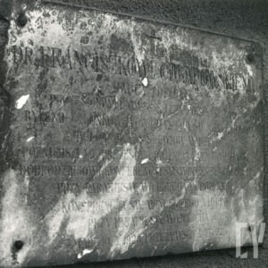 zniszczona, kamienna tablica z napisami przytwierdzona do muru
