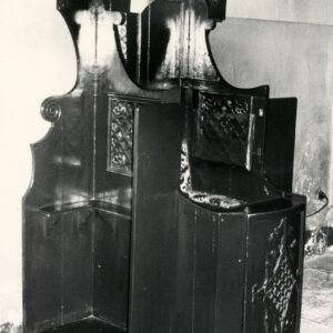 konfesjonał z ciemnego drewna ze zdobieniami i wzorzystym, wyściełanym siedziskiem