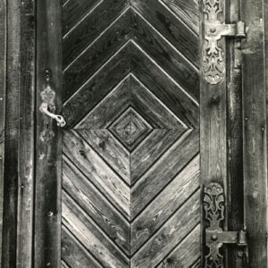 drewniane drzwi z ukośnie ciętych desek z żelaznymi, ozdobnymi zawiasami i klamką