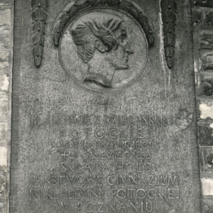 kamienna tablica z płaskorzeźbionym portretem kobiety z profilu i napisami przytwierdzona do muru
