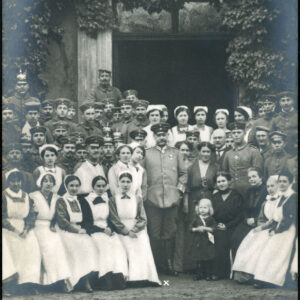 grupa kobiet i mężczyzn pozujących do zdjęcia na tle budynku porośniętego bluszczem; mężczyźni noszą mundury wojskowe; większość kobiet w strojach sióstr szpitalnych