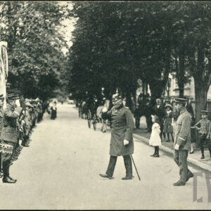 czarno-biała fotografia przedstawiająca starszego mężczyznę w mundurze oficerskim i pikielhaubie, salutującego przed grupą młodych ludzi w uniformach, część z nich gra na instrumentach 