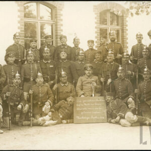 grupa mężczyzn w mundurach, z szablami i karabinami, przed budynkiem z cegieł