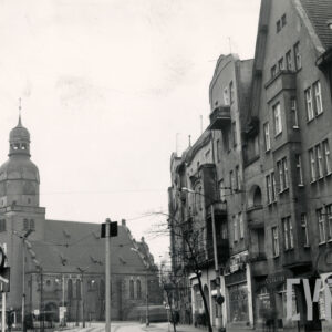 z prawej kilkukondygnacyjne kamienice wzdłuż ulicy, w głębi kościół z wieżą