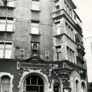 czterokondygnacyjna kamienica z poddaszem i zdobionym detalem architektonicznym nad łukowatym oknem na parterze