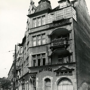 czterokondygnacyjna kamienica z poddaszem i zdobionym szczytem z wieżyczkami i balkonami