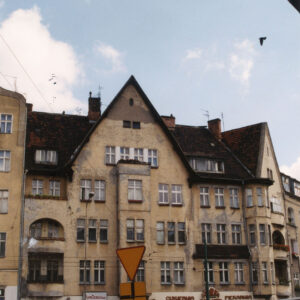 trzypiętrowa kamienica z mieszkalnym poddaszem i trójkątnym szczytem, przed kamienicą ruch uliczny