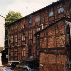 dwupiętrowy budynek drewniano-ceglany z niższą przybudówką i płaskim dachem