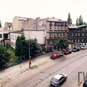kilkukondygnacyjne budynki i kamienice, na pierwszym planie ulica z torami tramwajowymi, wzdłuż niej, po obu stronach zaparkowane samochody