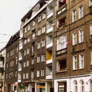 kilkukondygnacyjne budynki z balkonami, na pierwszym planie ulica z torami tramwajowymi