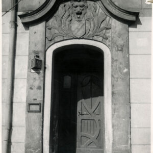 drewniane drzwi nad nimi bogata dekoracja rzeźbiarska, przed drzwiami kamienne schodki