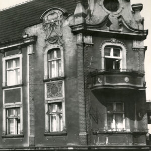 fragment elewacji kamienicy zakończony zdobionym szczytem, na narożniku balkony