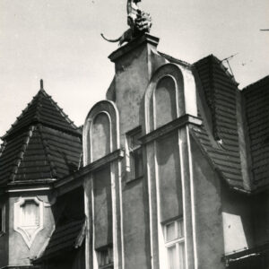 zdobionym szczyt kamienicy z rzeźbą przedstawiającą mężczyznę z uniesioną dłonią, tryumfującego nad lwem