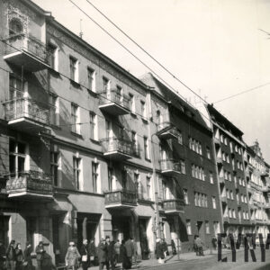 kilkukondygnacyjne budynki mieszkalne, przed budynkiem przystanek tramwajowy i czekający na tramwaj ludzie