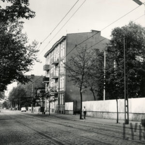 trzypiętrowa kamienica, na pierwszym brukowana ulica z torami tramwajowymi