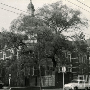 budynek w formie pałacyku z wieżyczką nakrytą hełmem, na pierwszym planie duże drzewo przysłaniające budynek