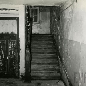 z lewej drewniane odrapane drzwi, z prawej drewniane schody, na ścianach odchodząca farba