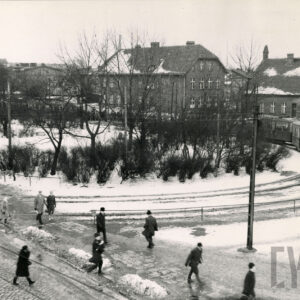 pętla tramwajowa w zimowej scenerii z lotu ptaka, w głębi dwa kilkupiętrowe, ceglane budynki, na pierwszym planie przechodzący ludzie, z prawej tramwaj
