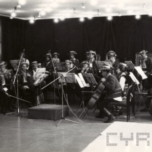 występ orkiestry, muzycy w strojach ludowych, z lewej solistka w stroju ludowym śpiewa do mikrofonu