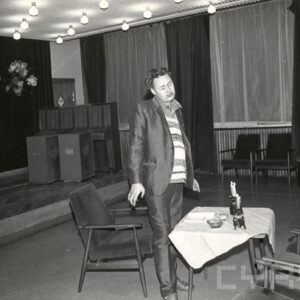 stojący mężczyzna, przed nim niski stolik, nakryty jasnym obrusem, na którym palą się świece